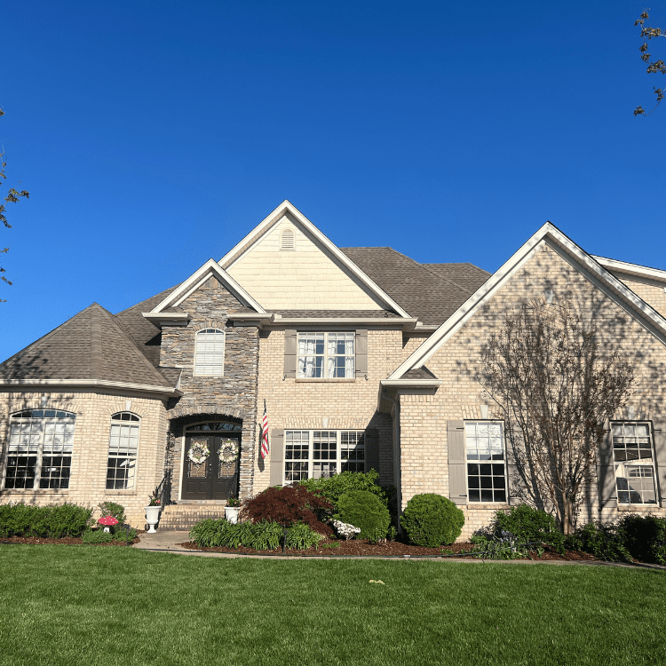 A large, elegant suburban home on a bright sunny day beneath a vivid blue sky.