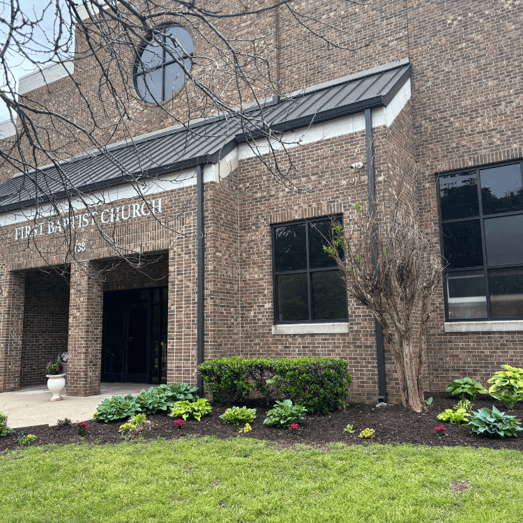 Exterior entrance of a large brick church building identified as First Baptist Church.