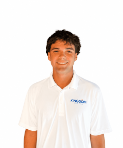 Young man wearing a white "Kingdom" polo shirt, standing and smiling against a plain white background.