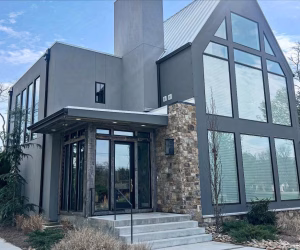 Modern two-story house with large windows, gray exterior, stone accent wall, and a small front porch with steps.