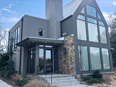 Modern two-story house with large windows, gray exterior, stone accent wall, and a small front porch with steps.