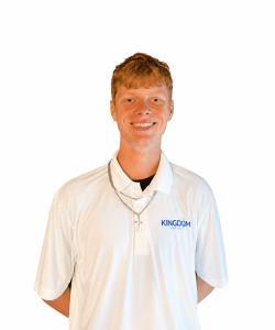 Young man in a white "KINGDOM" polo shirt and cross necklace, smiling at the camera against a plain background.