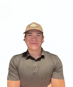 A young person wearing a brown cap and a dark polo shirt stands against a plain white background, arms loosely crossed.