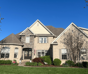 A large, elegant suburban home on a bright sunny day beneath a vivid blue sky.