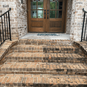 A brick front entryway with multiple steps leading to a set of elegant wooden double doors.