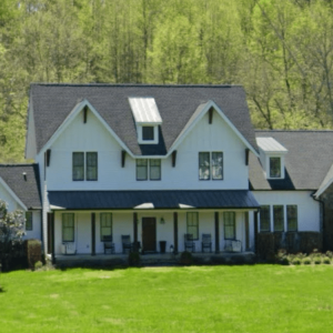 A modern farmhouse-style home surrounded by lush greenery and open lawn space.