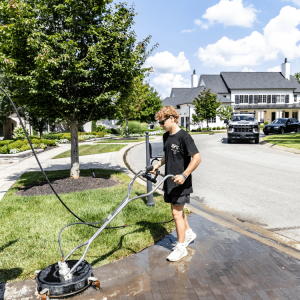 A young man professionally pressure washing a paved walkway or driveway.