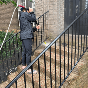 Person pressure washing brick stairs outside a house while wearing a rain jacket and sandals.