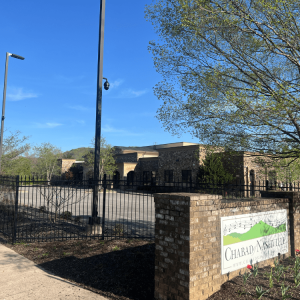 A brick sign for Chabad Nashville stands in front of a stone building and an empty parking lot on a clear day.
