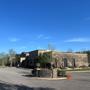 A brick building labeled "Genesis Campus for Jewish Life" with trees, an empty parking lot, and two orange cones.
