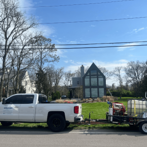 A white pickup truck with equipment is parked in front of a modern A-frame house on a sunny day.